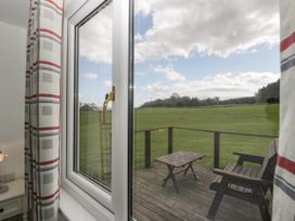 A window looking out to a wooden deck with a table and bench overlooking a grassy field at Twilight in Raglan