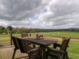 A wooden outdoor table with chairs on a deck overlooking a green field with grazing sheep at Twilight in Raglan