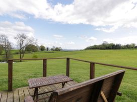 A wooden bench and table on a deck overlooking a grassy field with trees under a cloudy sky at Twilight in Raglan