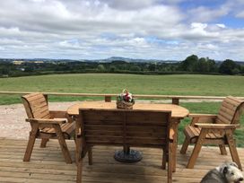 A wooden table with chairs on a deck overlooking a grassy field with a basket of flowers on the table at Twilight in Raglan