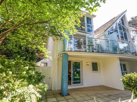 An exterior view of a house with a glass balcony and patio surrounded by trees and bushes at 6 Red Sails in Sandbanks