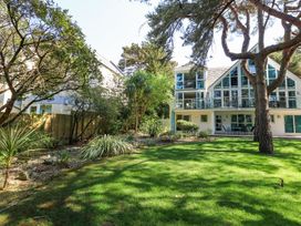 A garden with grass trees and shrubs in front of a house with large windows at 6 Red Sails in Sandbanks