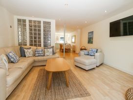 A living room with a beige sectional sofa, armchair, wooden coffee table, and a wall-mounted TV at 6 Red Sails in Sandbanks