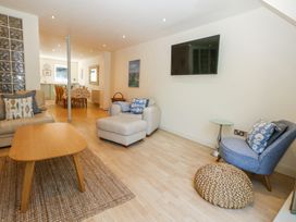 A living room with a beige sofa and armchair, wooden coffee table on a woven rug, blue chair with cushion, wall-mounted TV and dining table in the background at 6 Red Sails in Sandbanks