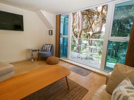 A living room with a sofa, wooden coffee table, armchair, side table, wall-mounted TV, and glass doors opening to a balcony with metal chairs and table at 6 Red Sails in Sandbanks