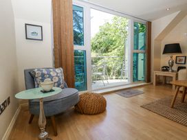 A living room with a blue chair and a small round table next to a sliding glass door leading to a balcony with metal chairs at 6 Red Sails in Sandbanks