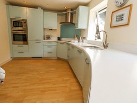 A kitchen with light green cabinets and drawers a built-in oven and microwave a stainless steel range hood and light wooden floor at 6 Red Sails in Sandbanks