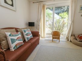 A living room with a patterned sofa and fish design cushions near sliding glass doors with a wicker chair and plants outside at 6 Red Sails in Sandbanks