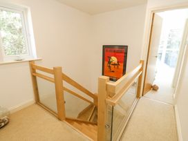 A staircase with wooden handrails and glass panels next to a hallway with a door and a framed poster on the wall at 6 Red Sails in Sandbanks