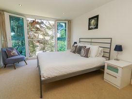 A bedroom with a bed with pillows a bedside table with a lamp a chair and large windows at 6 Red Sails in Sandbanks