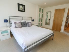 A bedroom with a double bed white bedding bedside tables lamps a wardrobe a wall mirror and a wooden door at 6 Red Sails in Sandbanks