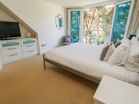 A bedroom with a bed facing large glass doors overlooking trees at 6 Red Sails in Sandbanks