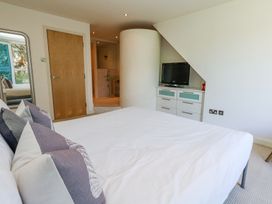 A bedroom with a bed and pillows a chest of drawers with a television on top and a door leading to a bathroom at 6 Red Sails in Sandbanks