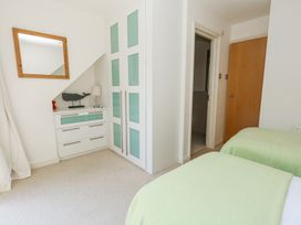 A bedroom with two single beds with green covers a white built in wardrobe a chest of drawers with a lamp and whale decoration and a wooden door at 6 Red Sails in Sandbanks