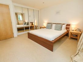 A bedroom with a wooden bed, two side tables with lamps, mirrored wardrobe doors, and a carpeted floor at 6 Red Sails in Sandbanks