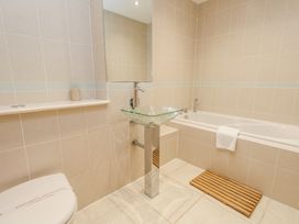 A bathroom with a glass sink on a metal pedestal bathtub with a towel and wooden mat on the floor at 6 Red Sails in Sandbanks