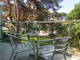 A balcony with two metal chairs and a round table with two cups overlooking trees and greenery at 6 Red Sails in Sandbanks