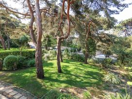 A garden with grass lawn trees and shrubs surrounded by a pathway and a wall at 6 Red Sails in Sandbanks