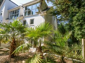 The rear exterior of a white two story house with large windows and tropical plants in the garden at 6 Red Sails in Sandbanks