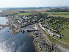 An aerial view of a coastal village with fields and a pier at Puffin Cottage in Craster