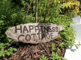 A wooden sign that reads Happiness Cottage in a garden at Happiness Cottage Piddlehinton