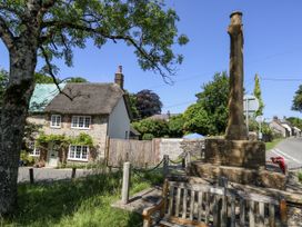A house with a thatched roof and a memorial in front at Happiness Cottage in Piddlehinton