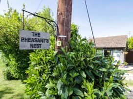 A wooden sign reading The Pheasant's Nest hanging from a wooden pole amidst green bushes with a small building in the background at The Pheasant's Nest in Welland near Upton Upon Severn