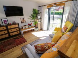 A living room with a yellow armchair a gray sofa decorative pillows a wooden chest of drawers a wall-mounted TV and glass doors open to outside at The Pheasant's Nest in Welland near Upton Upon Severn