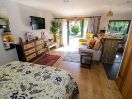 A room with a bed featuring a patterned cover a dresser with drawers a wall-mounted television a sofa with cushions a yellow armchair a wooden floor and a window overlooking a garden at The Pheasant's Nest in Welland near Upton Upon Severn