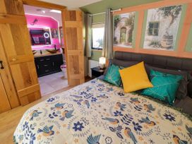 A bedroom with a bed and decorative pillows and a patterned bedspread next to a window and a door leading to a bathroom with a pink wall at The Pheasant's Nest in Welland near Upton Upon Severn