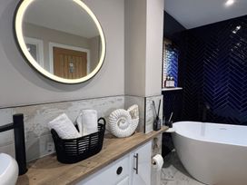 A bathroom with a bathtub and round mirror at Craster House Seahouses