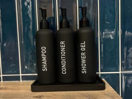 Bottles of shampoo, conditioner, and shower gel on a tray in a bathroom at Craster House in Seahouses