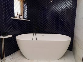 A bathroom with a bathtub and bottles on a shelf at Craster House, Seahouses