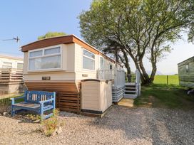 A mobile home with a small porch and stairs outside a large tree and a blue bench at No 29 Wyndham Hall in Cockermouth