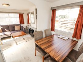 A living room with a gray sofa, wooden coffee table, dining table with chairs, and large windows with orange curtains at No 29 Wyndham Hall in Cockermouth