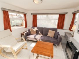 A living room with a gray sofa and beige chair near windows with red curtains at No 29 Wyndham Hall in Cockermouth