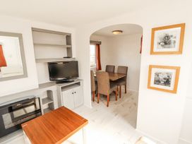 A living room with a TV on a stand a wooden table in front a fireplace and a dining area with chairs at No 29 Wyndham Hall in Cockermouth