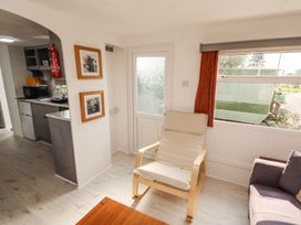 A living area with a wooden framed chair a window with red curtains and a small kitchen area in view at No 29 Wyndham Hall in Cockermouth