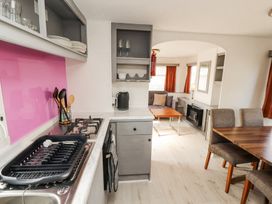 A kitchen with a stove and dishes next to a dining table with chairs and a small living area with a sofa and table at No 29 Wyndham Hall in Cockermouth
