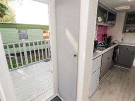 A small kitchen with grey cabinets a stove sink and a refrigerator next to an open door leading to a white deck with railing at No 29 Wyndham Hall in Cockermouth