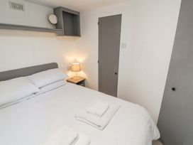 A bedroom with a bed white bedding two folded towels on the bed a bedside table with a lamp and a closed door at No 29 Wyndham Hall in Cockermouth