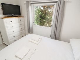 A bedroom with a bed folded towels a white chest of drawers with a television by a window with grey curtains at No 29 Wyndham Hall in Cockermouth