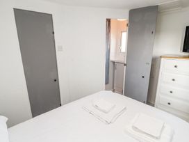 A bedroom with a bed holding folded white towels two grey doors one open showing a bathroom and a white dresser with drawers at No 29 Wyndham Hall in Cockermouth