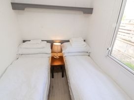 A small bedroom with two single beds separated by a wooden nightstand with a lamp and a window on the right side at No 29 Wyndham Hall in Cockermouth