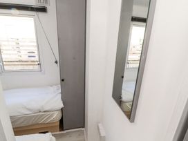 A small bedroom with a single bed under a window and a tall gray cupboard beside it along with a wall mirror in No 29 Wyndham Hall Cockermouth