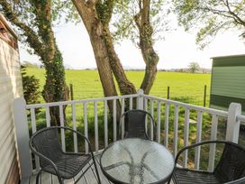 A small outdoor deck with a glass table and three chairs overlooking a grassy field at No 29 Wyndham Hall in Cockermouth