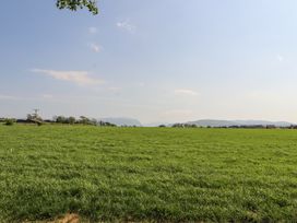 A large green field with some trees and buildings in the distance under a clear sky at No 29 Wyndham Hall in Cockermouth
