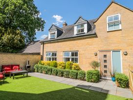 A patio area with a wooden table and red cushioned chairs next to a stone house with windows and shrubs at The Coach House in Castle Cary