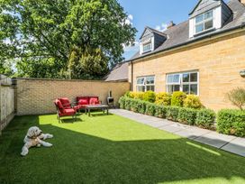 A garden with red outdoor chairs and a table a dog lying on grass and bushes along a house wall at The Coach House in Castle Cary