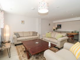 A living room with beige sofas a wooden coffee table a floor lamp a TV on a stand and a dining table with chairs at The Coach House in Castle Cary
